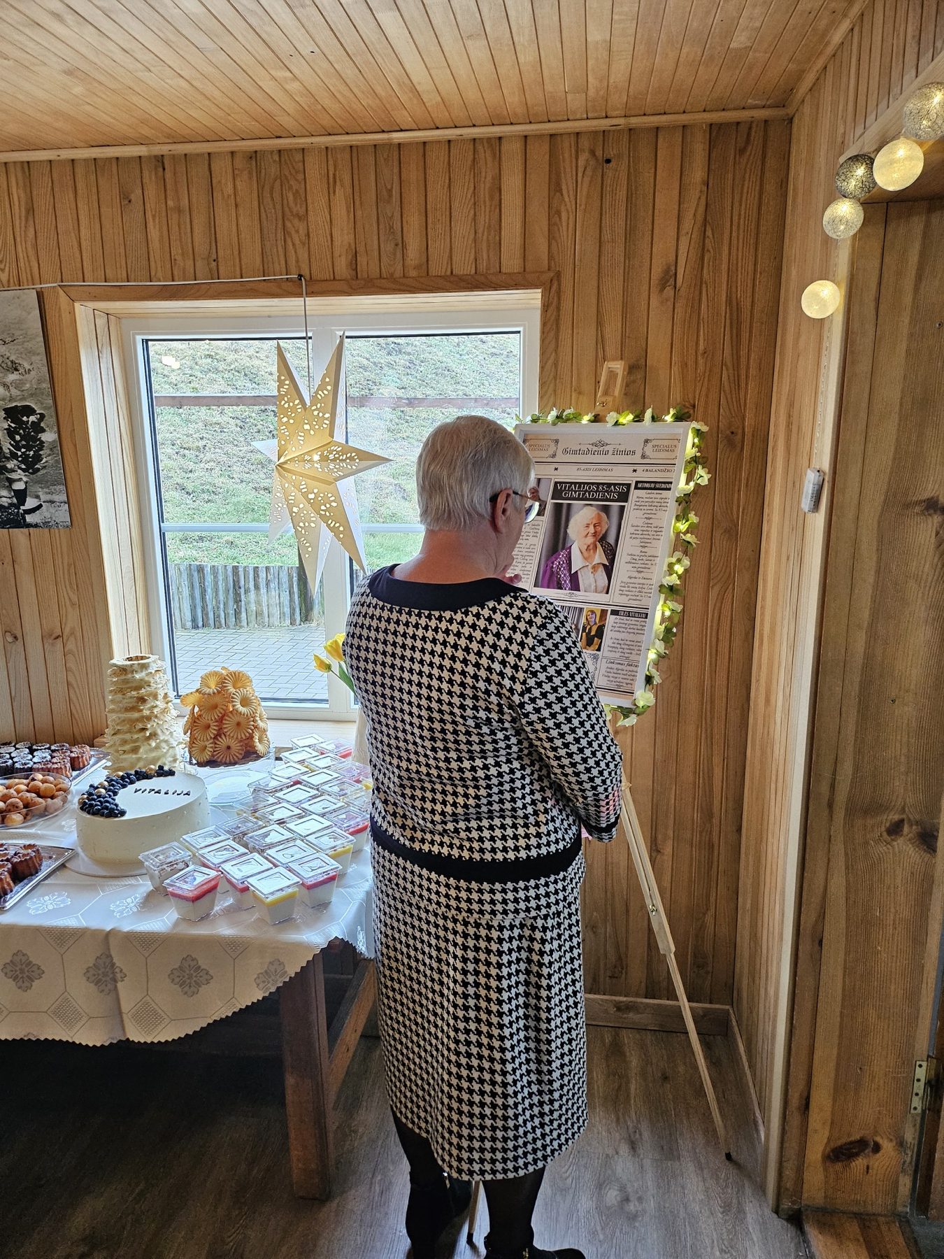 Močiutė skaito įrėmintą šeimos laikraštį, padovanotą 85-ojo gimtadienio proga
